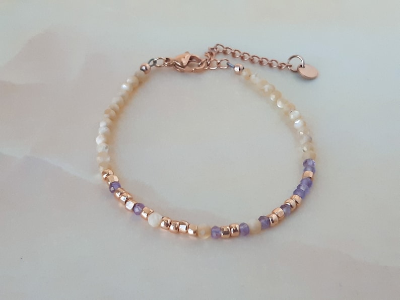 K&ouml;nnte beinhalten: Ein zartes Armband mit einer Mischung aus wei&szlig;en und gelben Perlen, akzentuiert mit kleinen lila Perlen und einem ros&eacute;goldenen Verschluss.