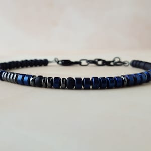 May include: A beaded bracelet with black and blue beads. The bracelet has a silver clasp.