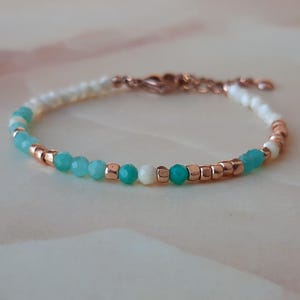 May include: A delicate bracelet with a gradient of turquoise and white beads, interspersed with small gold beads. The bracelet has a rose gold clasp.