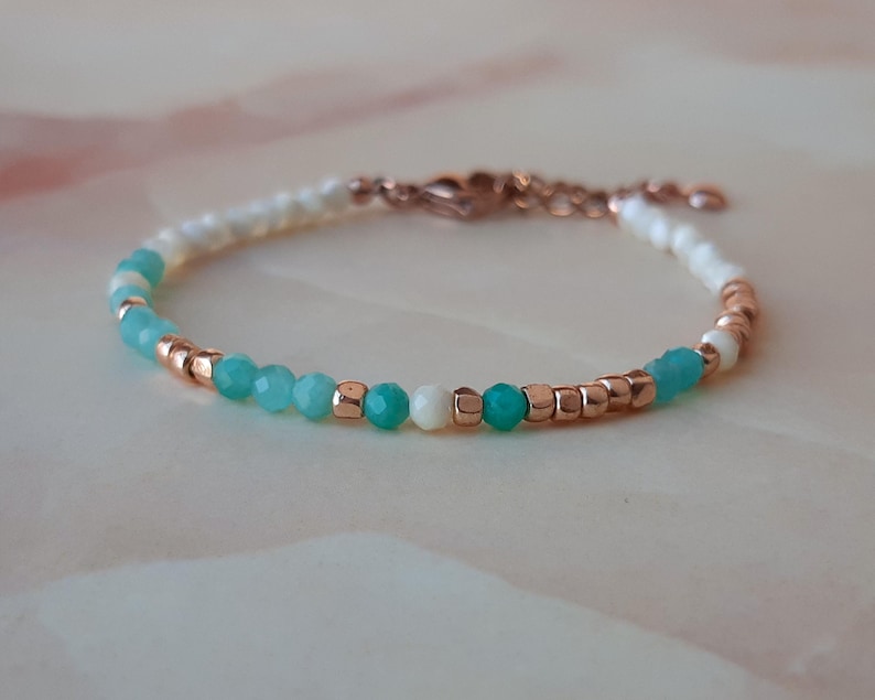 May include: A delicate bracelet with a gradient of turquoise and white beads, interspersed with small gold beads. The bracelet has a rose gold clasp.