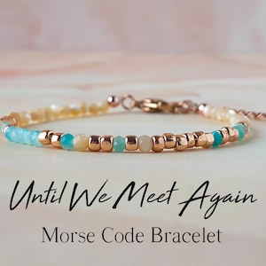 Puede incluir: Un brazalete delicado hecho con pequeñas cuentas en tonos crema, turquesa y oro rosa. El brazalete tiene un cierre y una cadena extensora. El texto "Until We Meet Again Morse Code Bracelet" está escrito debajo del brazalete.
