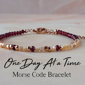 Può includere: Un braccialetto delicato con una catena in oro rosa e perline in tonalità rosso, bianco e oro. Il braccialetto presenta il messaggio "One Day At a Time" in codice Morse.