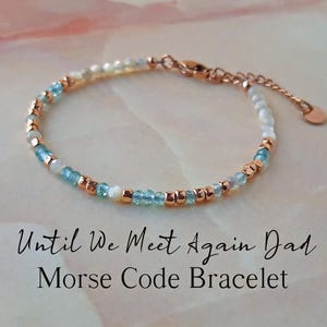 May include: A delicate bracelet made with blue and white beads and rose gold accents. The bracelet has the text "Until We Meet Again Dad" and "Morse Code Bracelet" on a white background.