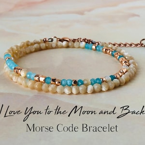 Puede incluir: Un brazalete de doble cadena con un mensaje en código Morse. El brazalete está hecho con cuentas de color azul claro y crema y separadores de color dorado. El texto de la imagen dice "I Love You to the Moon and Back Morse Code Bracelet".