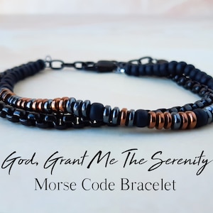 May include: A black, copper, and silver beaded bracelet with a black chain clasp. The bracelet has the text "God, Grant Me The Serenity" in Morse code.