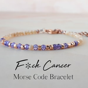 Könnte beinhalten: Ein zartes Armband mit einem Farbverlauf aus hellbeigen und violetten Perlen. Das Armband besteht aus kleinen, runden Perlen und hat einen roségoldenen Verschluss. Der Text "F*ck Cancer Morse Code Bracelet" steht unter dem Armband.