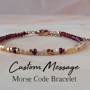 Könnte beinhalten: Ein zartes Armband mit einer individuellen Botschaft in Morsecode. Das Armband besteht aus kleinen roten, weißen und goldenen Perlen.
