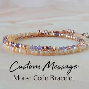 Peut inclure: Un bracelet délicat à double rang de perles de couleur claire et de perles violettes entrecoupées de perles en or rose. Le bracelet est doté d'un fermoir et d'un charme. Le texte "Custom Message Morse Code Bracelet" est situé sous le bracelet.