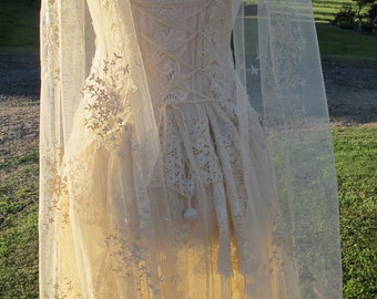 May include: A white lace dress with a sheer overlay and floral embroidery. The dress has a fitted bodice and a flowing skirt.