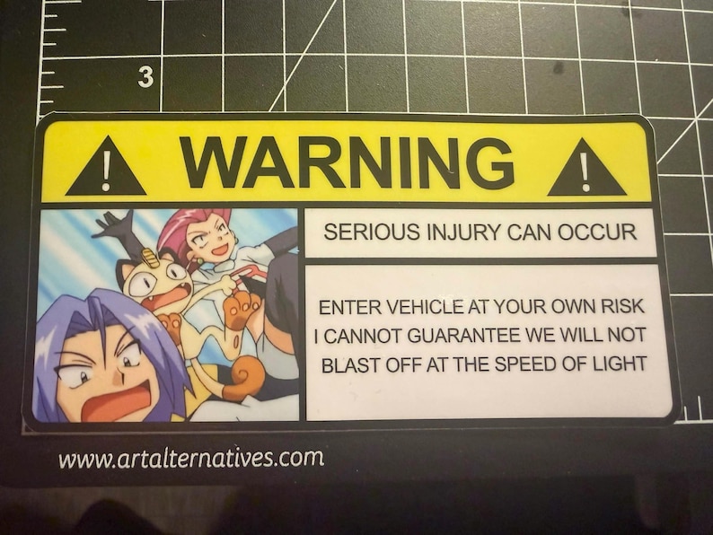 May include: A rectangular yellow and white warning sticker featuring an illustration of three cartoon characters from the Pokemon series. The text reads WARNING, SERIOUS INJURY CAN OCCUR, and ENTER VEHICLE AT YOUR OWN RISK I CANNOT GUARANTEE WE WILL NOT BLAST OFF AT THE SPEED OF LIGHT.