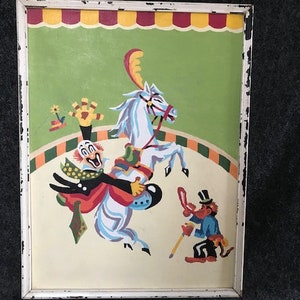 May include: A vintage framed painting of a clown riding a white horse in a circus ring. The clown is wearing a red, yellow, and blue costume and a white hat. A small figure of a monkey in a red and blue costume is standing to the right of the horse.