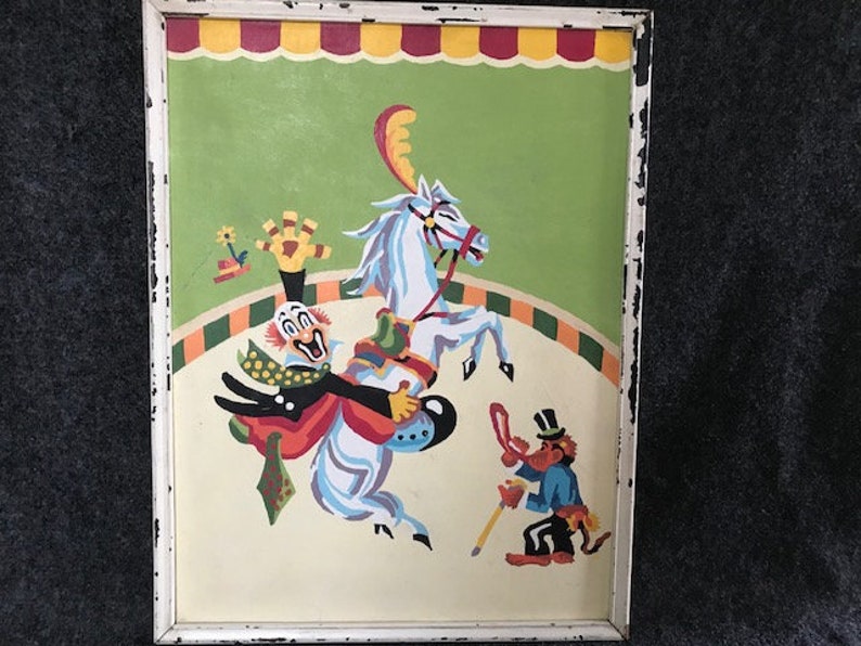 May include: A vintage framed painting of a clown riding a white horse in a circus ring. The clown is wearing a red, yellow, and blue costume and a white hat. A small figure of a monkey in a red and blue costume is standing to the right of the horse.