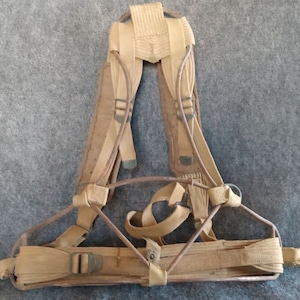 May include: A tan canvas military backpack frame with metal supports and straps. The frame is designed to hold a backpack or other gear.