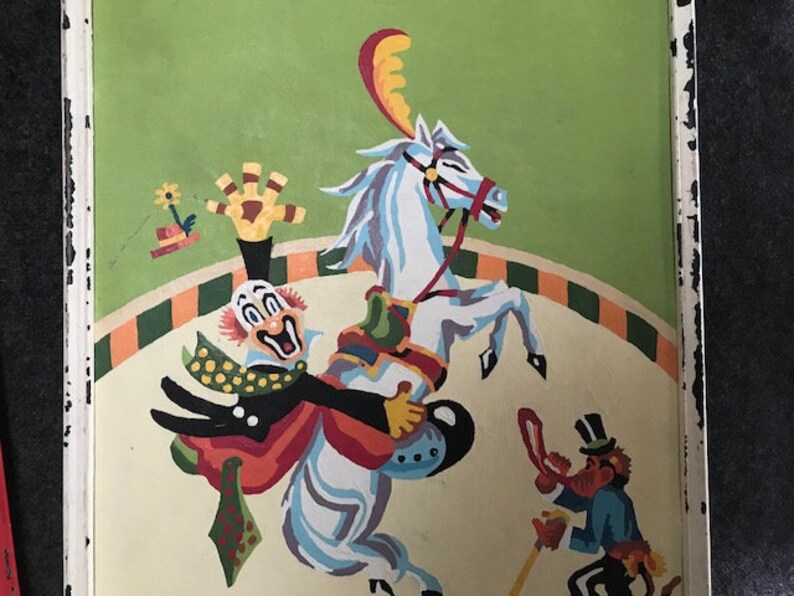 May include: A colorful painting of a clown riding a white horse in a circus ring. The clown is wearing a red, yellow, and green costume and has a big smile. The horse is wearing a red and yellow saddle and has a red bridle. There is a small figure of a monkey in the background.