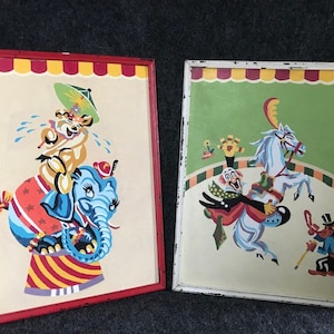 May include: Two framed vintage paint-by-number pictures with circus themes. The first picture shows a crying lion riding a blue elephant on a red and white striped platform. The second picture shows a clown riding a white horse with a red and white striped saddle. A man with a top hat and cane stands to the right.