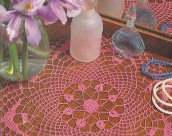 Peut inclure: Nappe en crochet rose avec un motif floral sur une surface en bois. L'image présente également un vase d'iris violets, des flacons de parfum et des objets décoratifs, créant une esthétique vintage.