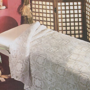 May include: White crocheted throw blanket with a delicate floral pattern. The blanket is draped over a white massage table.