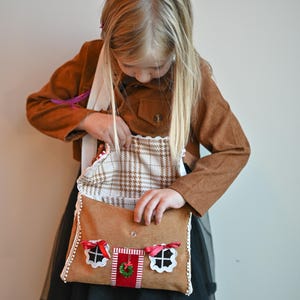 A girl is opening a Gingerbread House Christmas Purse – Peppermint Candy Holiday Crossbody Bag.