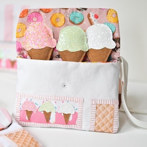 May include: A white fabric crossbody bag featuring a flap with a pink donut print lining. The flap displays three plush ice cream cones in pink, green, and white glitter. The front pocket shows three smaller ice cream appliques and a waffle texture.