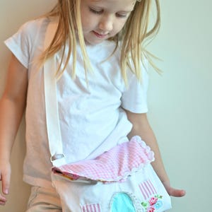 The girl is wearing a Fairy Cottage House Purse –  Crossbody Bag