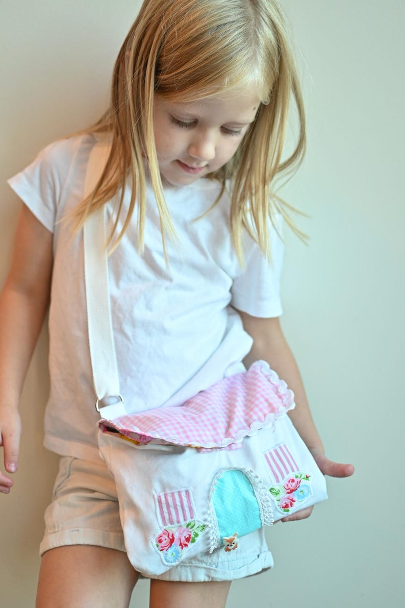 The girl is wearing a Fairy Cottage House Purse –  Crossbody Bag