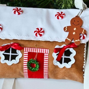 May include: A brown corduroy crossbody bag shaped like a gingerbread house. The white flap features red and white peppermint candy embellishments and a brown gingerbread man keychain. The bag has two windows with red bows and a red door with a wreath.