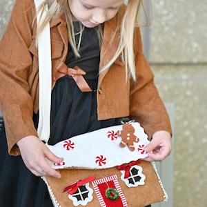 A girl is opening a Gingerbread House Christmas Purse – Peppermint Candy Holiday Crossbody Bag.