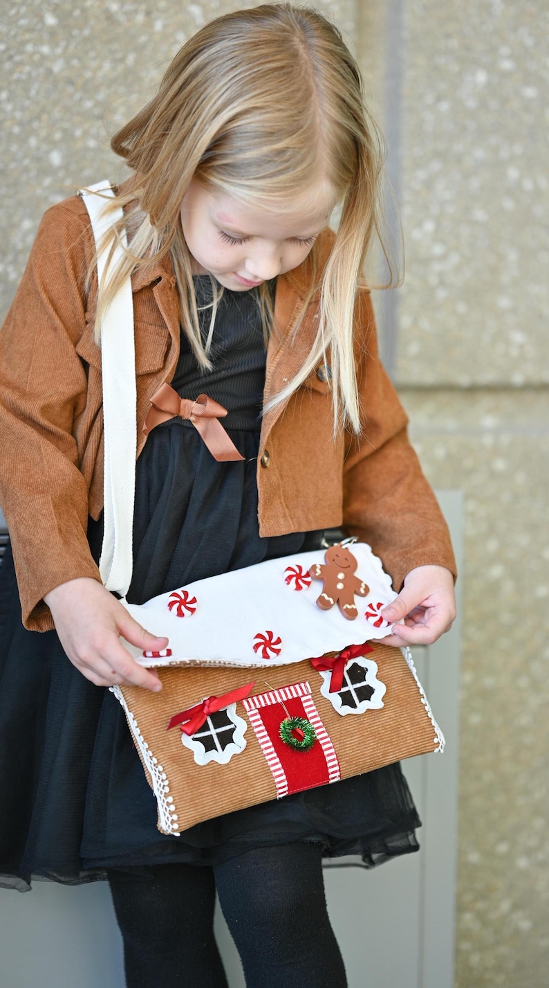 A girl is opening a Gingerbread House Christmas Purse – Peppermint Candy Holiday Crossbody Bag.