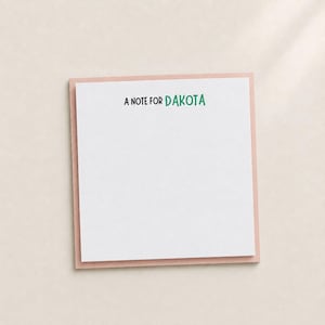 May include: A square notepad with a pale pink border and a white center. The text A NOTE FOR DAKOTA is printed at the top in a simple font, with the words A NOTE FOR in black and the name DAKOTA in a bright green color on the white paper.