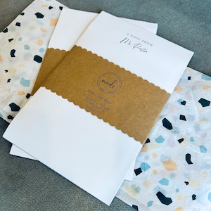 K&ouml;nnte beinhalten: Ein wei&szlig;er personalisierter Notizblock mit einer braunen Papierverpackung. Die Verpackung hat einen gewellten Rand und ein schwarz-wei&szlig;es Logo mit der Aufschrift "made creative group". Der Notizblock ist mit "Home and Host Personalized Notepad 5.5" W x 8.5" H 20 Sheets" beschriftet.