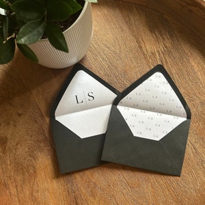 May include: Two black envelopes with white liners. The envelope on the left has the initials "LS" printed on the liner. The envelope on the right has a repeating pattern of the initials "LS" printed on the liner.