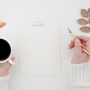 K&ouml;nnte beinhalten: Ein wei&szlig;es Blatt Papier mit dem Text "A note from Camille Wilson" oben. Eine Person h&auml;lt einen Stift und eine Tasse Kaffee.
