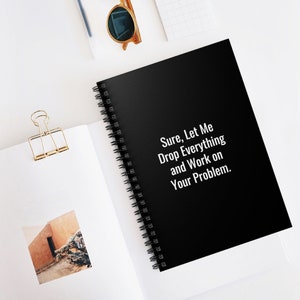 May include: A black spiral notebook with the text "Sure, Let Me Drop Everything and Work on Your Problem." printed in white on the cover.