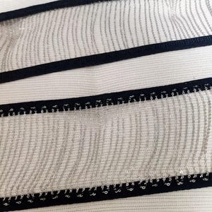 May include: Close-up of a black trim with silver chain fringe. The fringe is made of many small, linked chains.