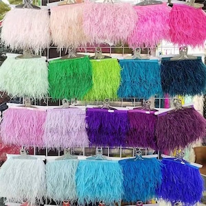 May include: Assortment of feather trim in various colors, including pink, green, blue, purple, and white. The feather trim is displayed on a wire rack.