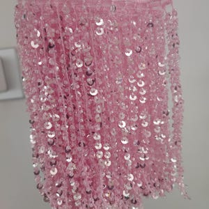 May include: Pink sequined fringe trim with a delicate, shimmering texture. The fringe is made of small, round sequins that are sewn onto a thin, flexible thread. This trim is perfect for adding a touch of sparkle and glamour to any project.