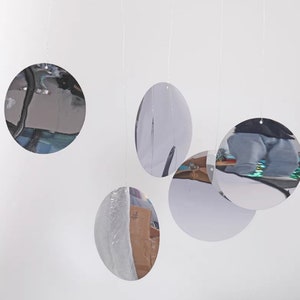Op de afbeelding: Een set van vijf zilveren, ronde en ovale, reflecterende hangende ornamenten. De ornamenten hangen aan witte touwtjes.