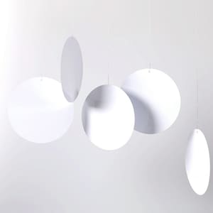 May include: Five white paper circles of varying sizes hanging from white strings against a white background. The circles are suspended at different heights.