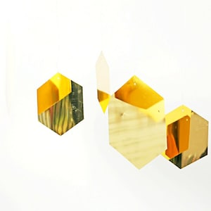 Op de afbeelding: Gouden, honingraatvormige papieren decoraties die aan een wit plafond hangen. De decoraties zijn gemaakt van glanzend goudpapier en zijn in een verspringend patroon gerangschikt.