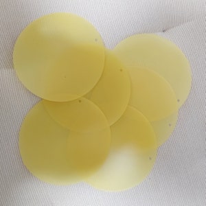 May include: A set of six yellow, round, fabric sequins with a hole in the centre.