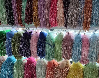 May include: A selection of beaded tassels in a variety of colours, such as green, blue, pink, and gold. Each tassel is attached to a small cap, creating a decorative and textured appearance. These tassels are likely used for crafting or embellishment.