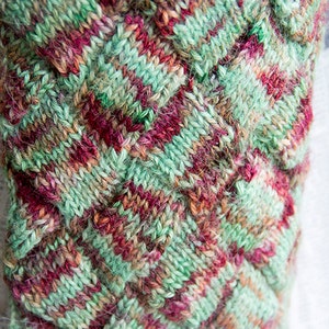 May include: Close-up of a knitted fabric with a green, red and brown colour scheme. The fabric has a textured, woven pattern.