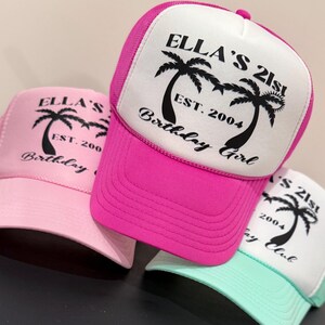 May include: Three pink, white and turquoise trucker hats with black palm tree graphics and the text "Ella's 21st", "Est. 2004", "Birthday Girl" and "Birthday Club".