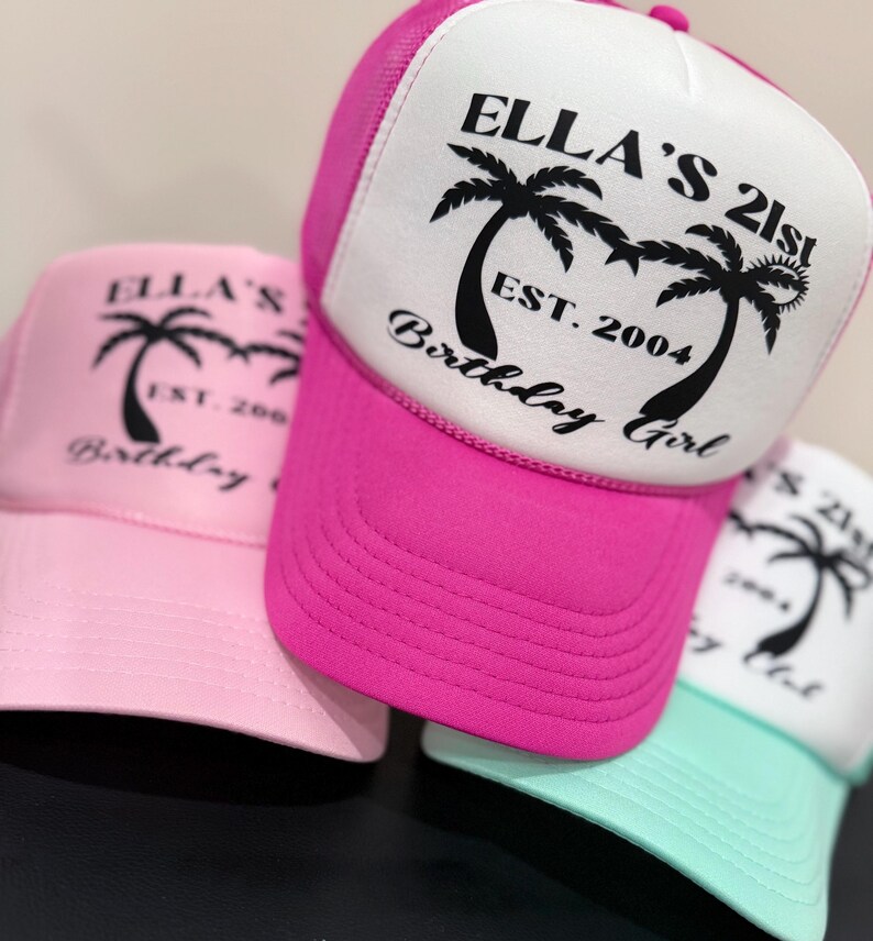 May include: Three trucker hats with pink, white and light blue mesh backs. The front of the hats are white with black palm trees and the text "Ella's 21st Birthday Girl Est. 2004".
