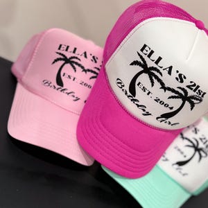 May include: Three trucker hats in pink, white and teal with black palm tree graphics and the text "Ella's 21st Birthday Girl Est. 2004".