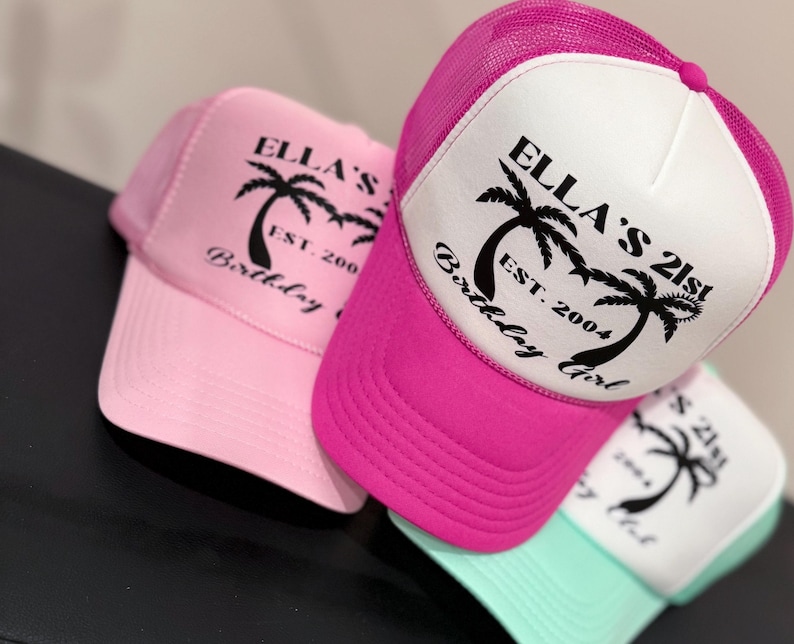 May include: Three trucker hats in pink, white and teal with black palm tree graphics and the text "Ella's 21st Birthday Girl Est. 2004".