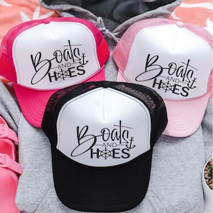 May include: Three trucker hats with a white front and black mesh back. The hats have a black graphic that says "Boats and Hoes" with an anchor and a compass.
