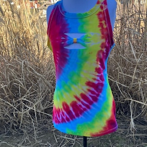 May include: A tie-dye tank top in a vibrant rainbow of colors, including red, yellow, blue, and green. The top features a unique bow-shaped cutout detail at the chest. The ribbed fabric adds texture to the colorful design.