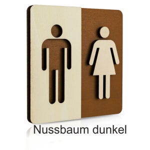 Puede incluir: Un letrero de madera con un s&iacute;mbolo masculino y femenino, separados por una l&iacute;nea vertical. El lado izquierdo es de madera clara y el lado derecho de madera oscura. El texto "Nussbaum dunkel" est&aacute; impreso debajo del letrero.