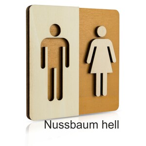 Puede incluir: Un letrero de madera con un s&iacute;mbolo masculino y femenino recortado. El letrero est&aacute; dividido en dos, con el s&iacute;mbolo masculino a la izquierda y el s&iacute;mbolo femenino a la derecha. El lado izquierdo es de madera clara y el lado derecho es de madera m&aacute;s oscura. El letrero dice "Nussbaum hell" en la parte inferior.